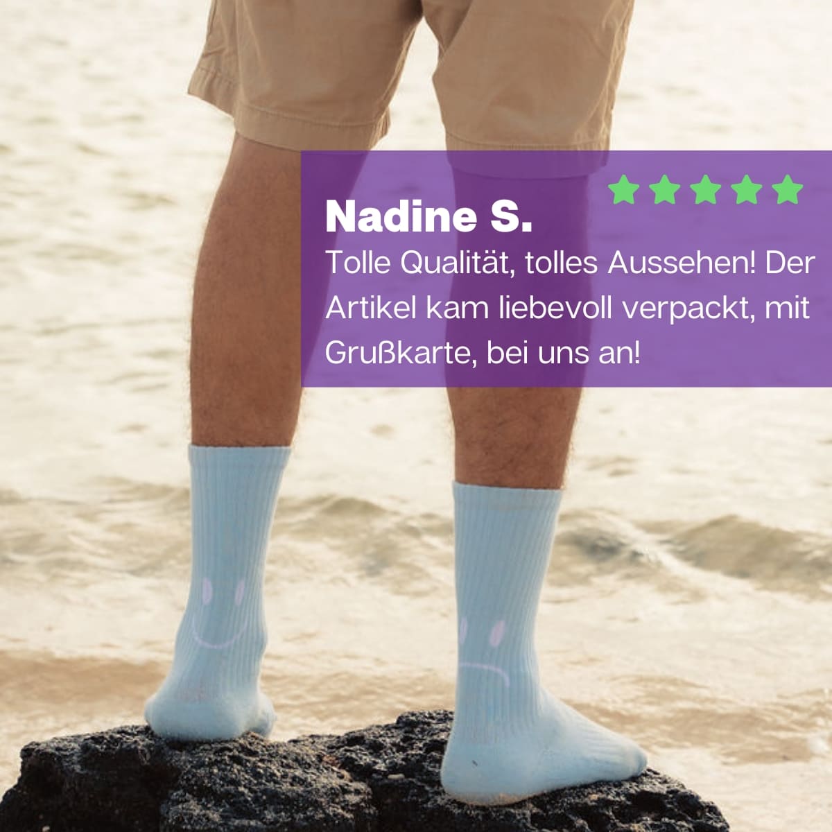 Mann stehend auf einem großem Stein am Strand mit hellblauen Sportsocken mit Smile Motiv von PATRON SOCKS