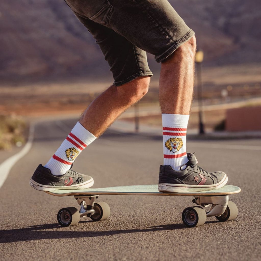 Mann steht auf Skateboard in Sport Socken mit Löwenkopf von PATRON SOCKS